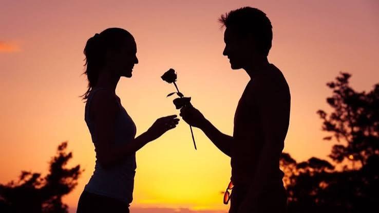 Silhouette of a couple at sunset as one offers the other a rose